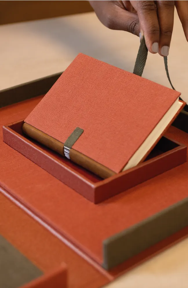 A hand lifting a small fabric-covered notebook from a gift box