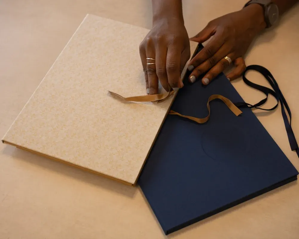 A person wrapping a gift with beige patterned paper and satin ribbons