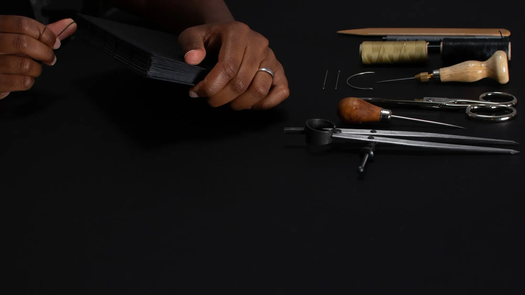 Hands binding a book, surrounded by bookbinding tools