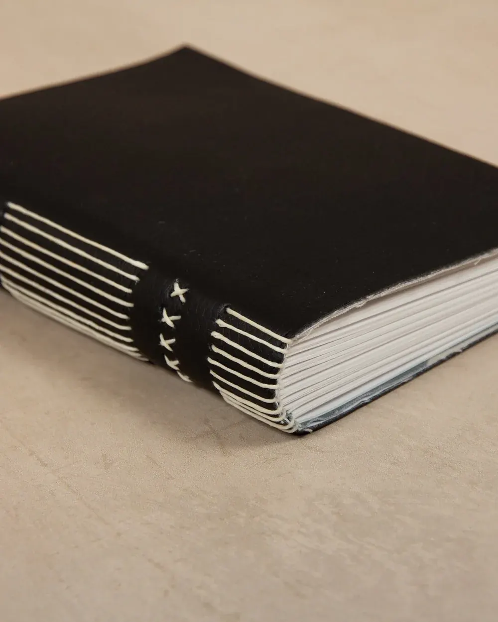 A black spiral-bound notebook with a black elastic band laced with white stitches, resting on a beige surface.