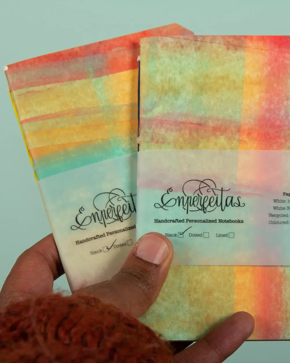 Close-up of a hand holding two watercolor-designed personalised notebooks, with options for blank, dotted, or lined pages