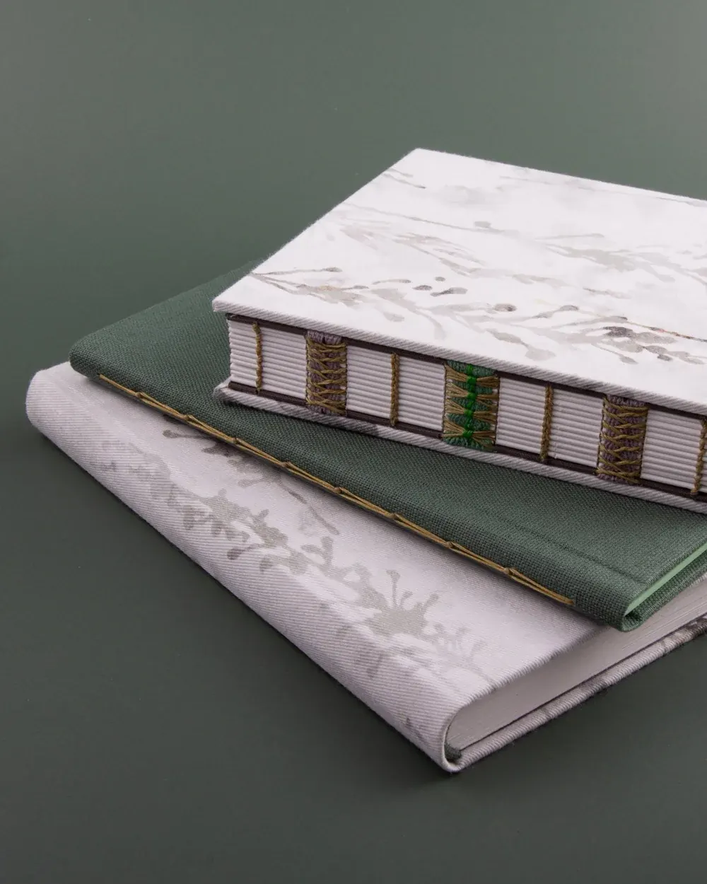 A stack of three books with decorative covers, placed on a green surface.