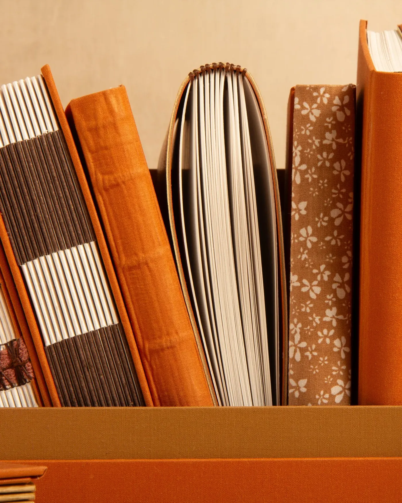 A row of orange and patterned notebooks on a shelf.