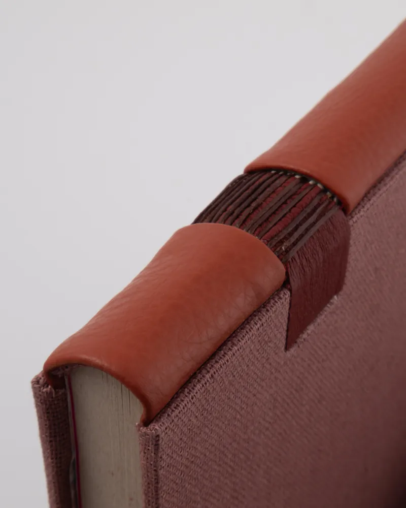 Close-up of a pink book with a leather spine and a decorative leather strap on the spine.