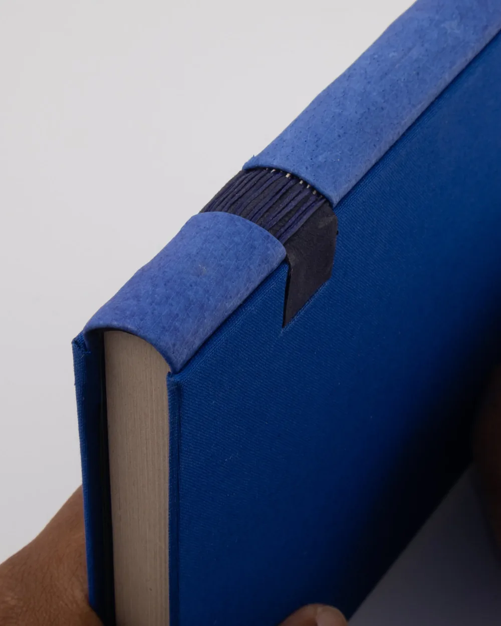 Close-up of the top corner of a blue hardcover book, showing the book's spine and cover with a blue fabric cover and a black tape reinforcement on the inner corner.