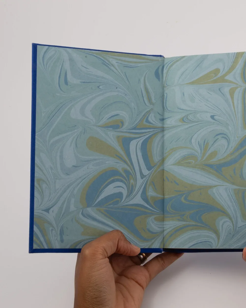 Open book with marbled paper pattern pages, held by person with dark skin, against a white background.