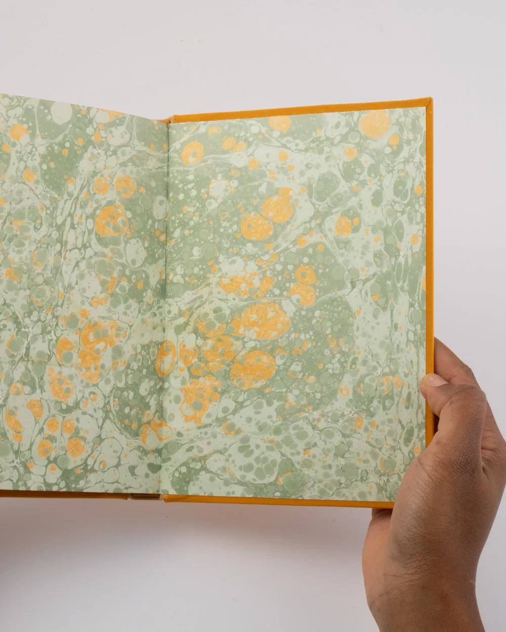 Open book with marbled green and orange pages held by a person's hand, against a white background.