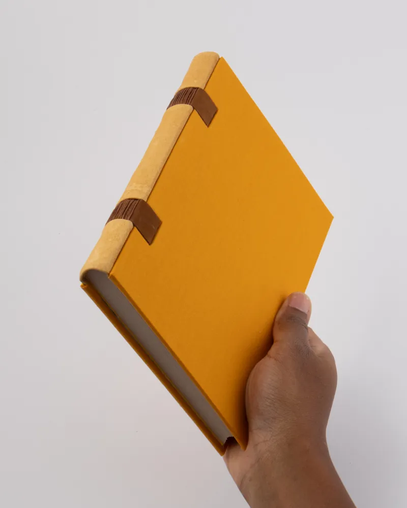 A person holding a hardcover yellow notebook with a textured cover and two brown loops on the spine.