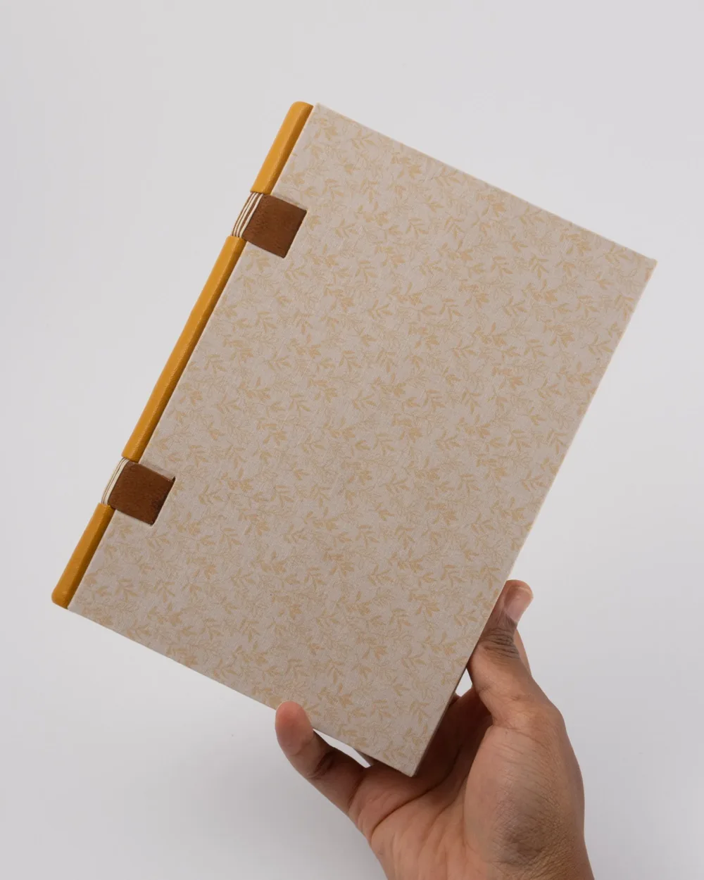 A person holding a beige patterned notebook with yellow and brown binding on a white background.