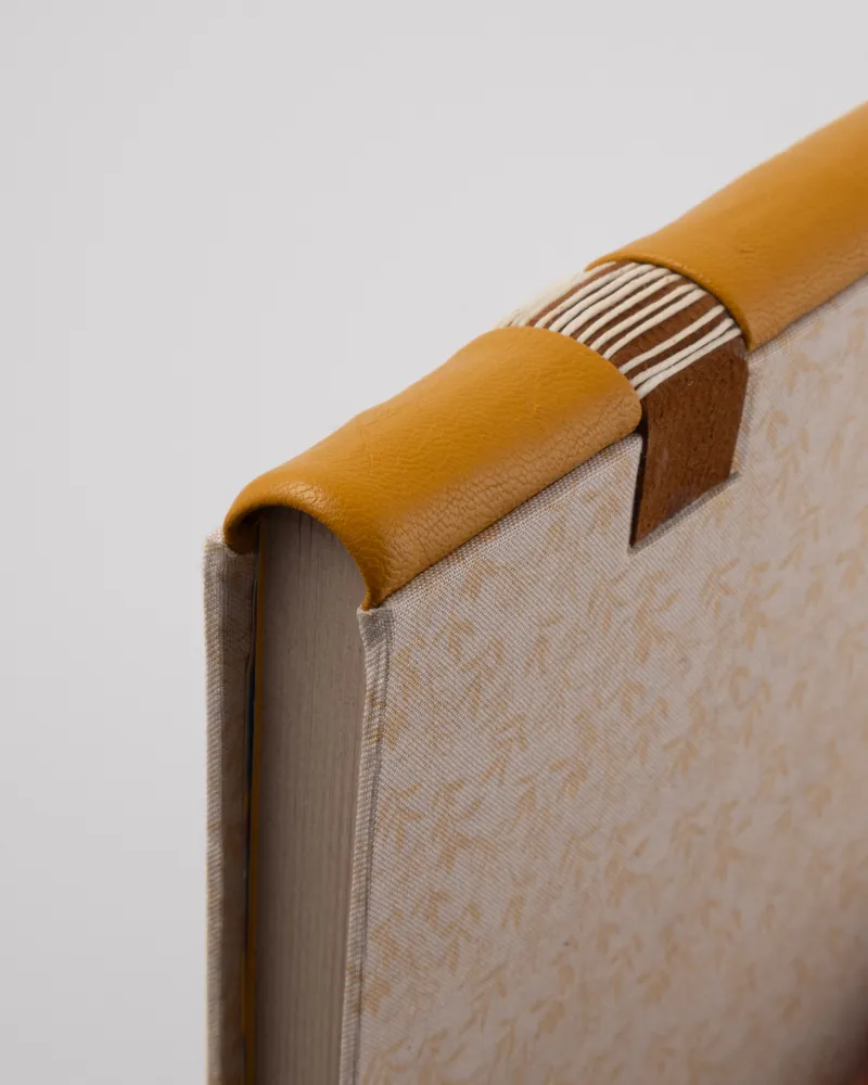 Close-up of a corner of a beige fabric-covered chair with a leather and wood decorative top edge in yellow and brown.