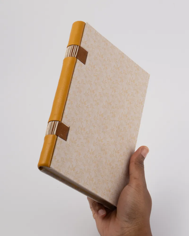 Person holding a patterned book with a yellow, brown, and striped spine against a plain white background.