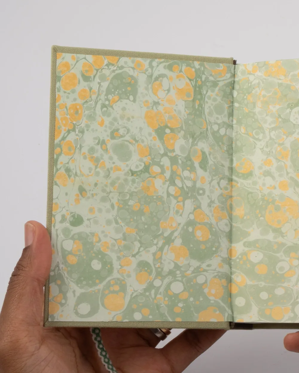 A person holding an open notebook with marbled paper pages in shades of green, yellow, and white.