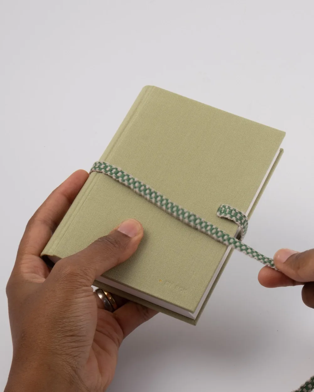 A person holding a light green notebook with a green and white elastic strap, on a white background.