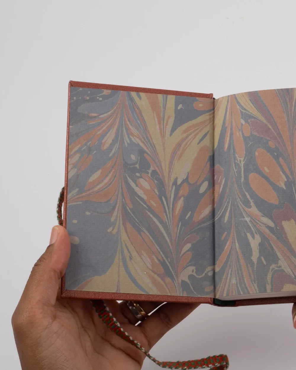 Open book with marbled paper pages and a red cover, being held by a hand, against a white background.
