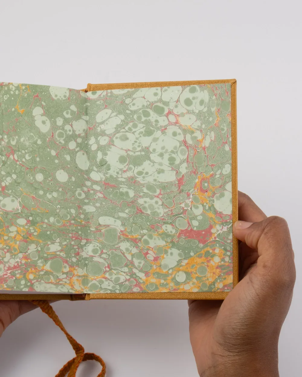 Person holding an open book with marbled green and pink pages against a white background.
