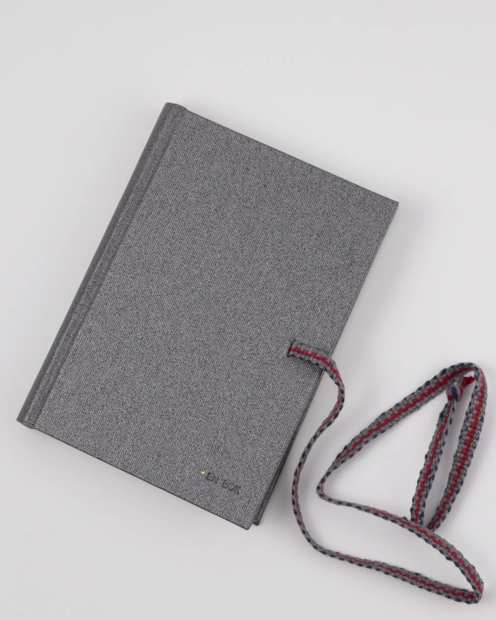 A closed gray fabric-textured notebook with a red, gray, and white striped elastic band and matching bookmark on a white background.