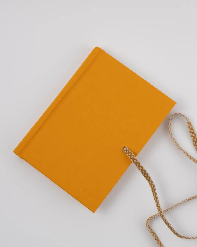A yellow hardcover book with a white and yellow braided string attached, resting on a white surface.