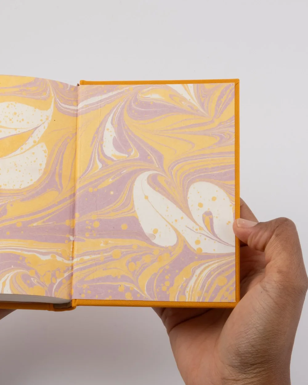 A person holding an open notebook with a marbled paper cover featuring yellow, purple, and white swirls and splashes.