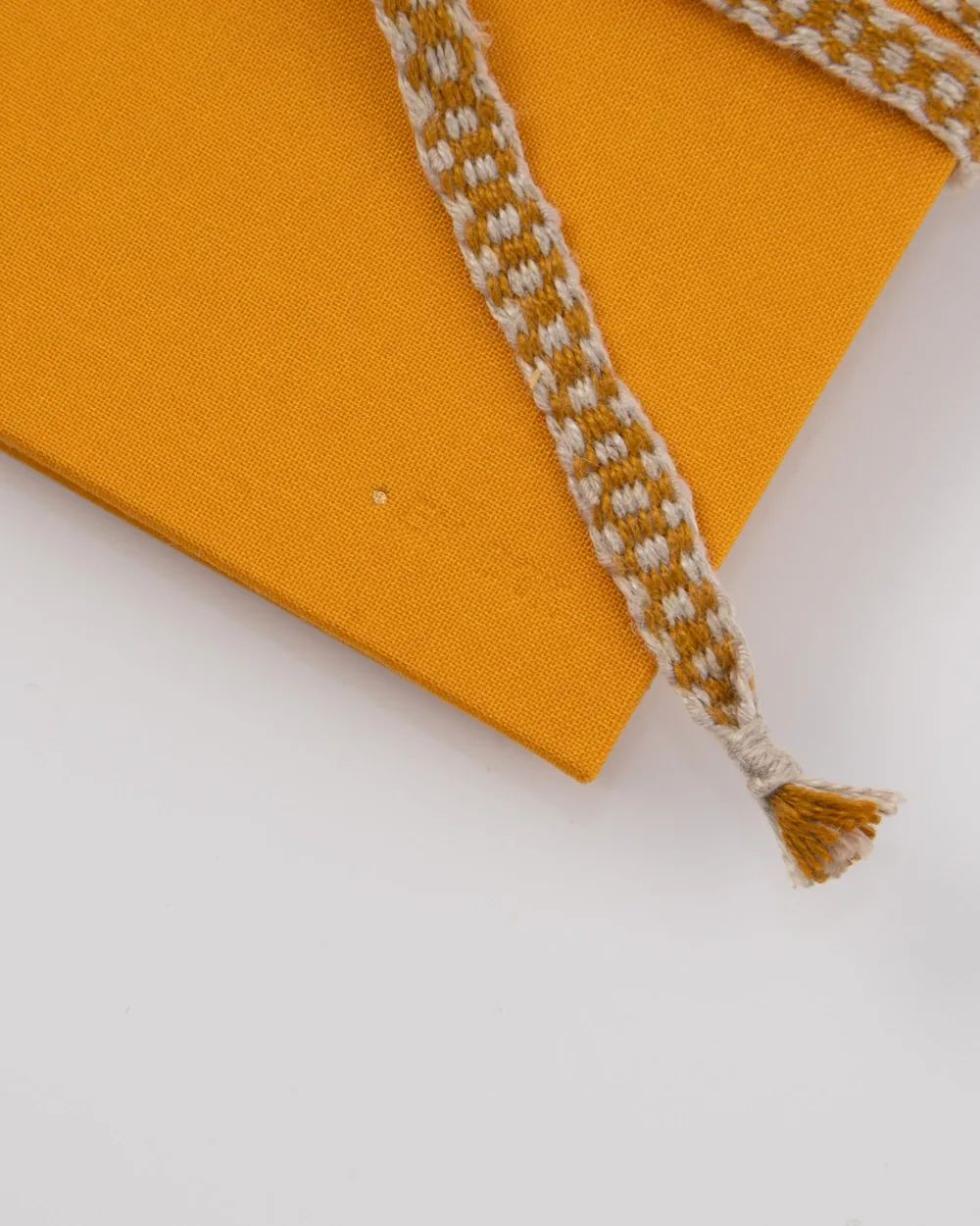 Close-up of a yellow fabric notebook with a yellow and white braided bookmark resting on it, on a white surface.