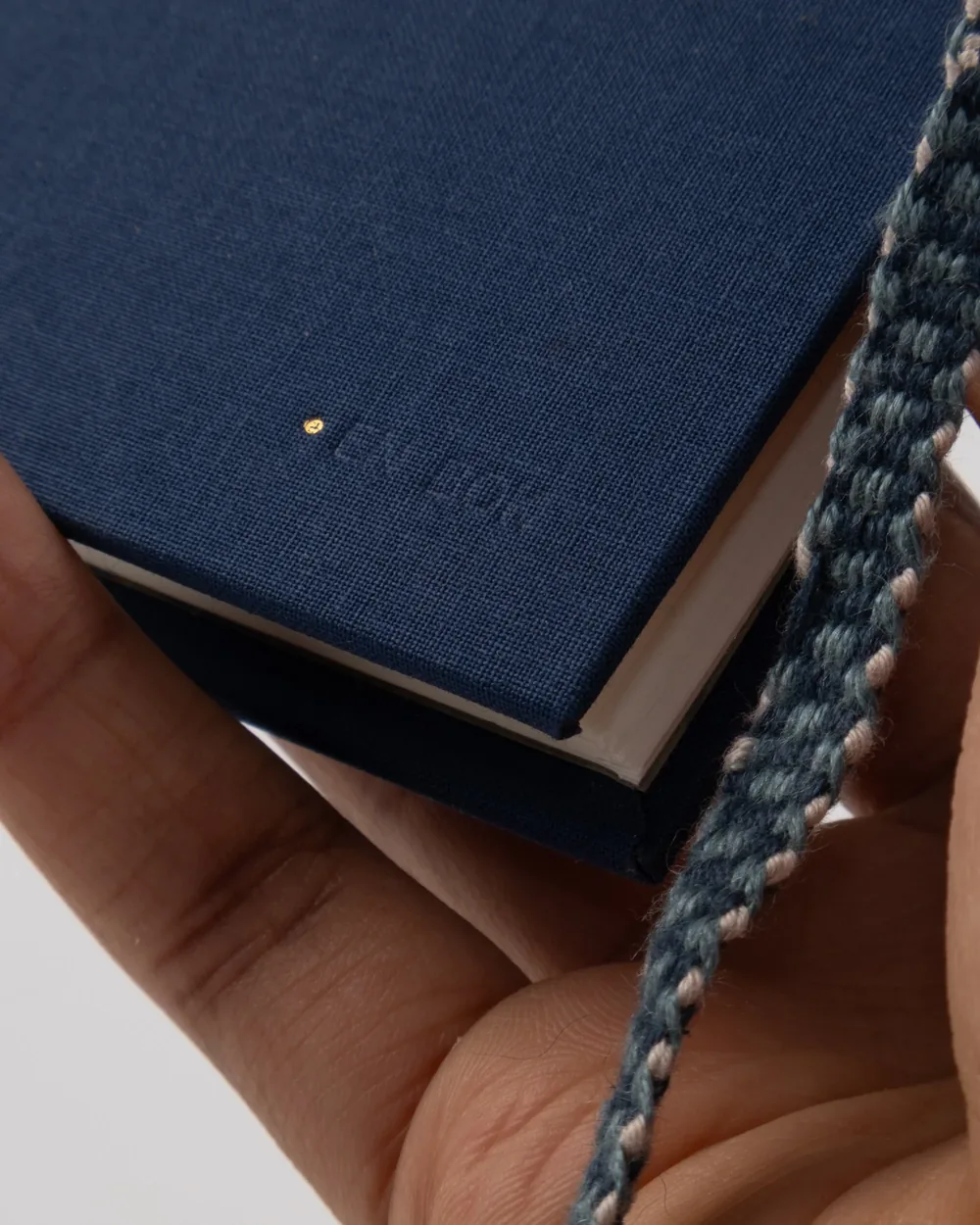Close-up of a blue hardcover notebook with the embossed word 'Notes' on the cover, held in a person's hand with a braided strap visible on the right side.