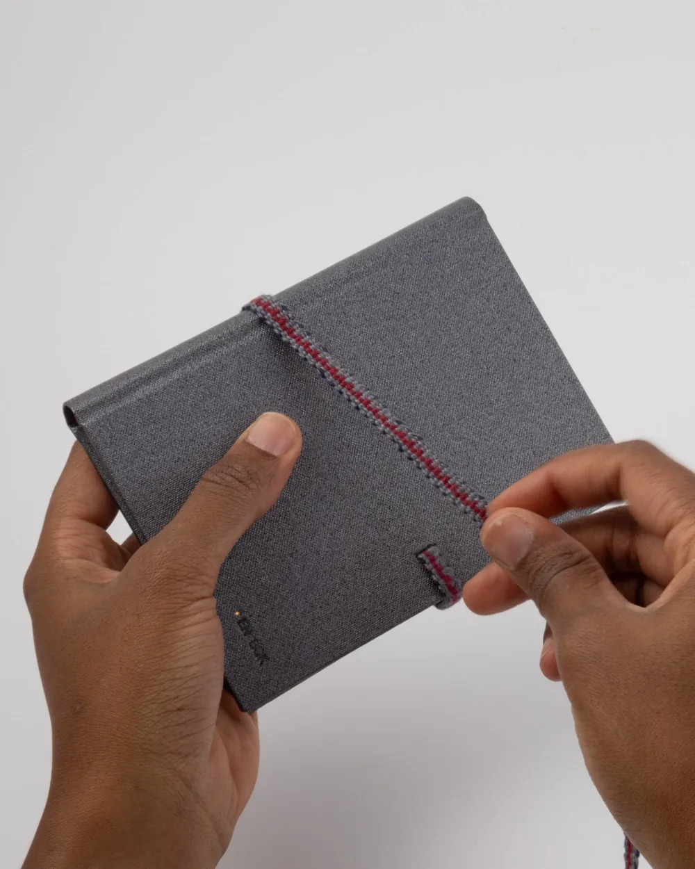 Person holding a gray fabric wallet with a red and black seam on a plain white background.