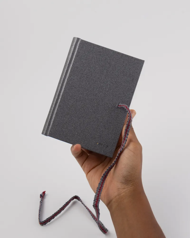 Person holding a gray fabric-covered notebook with a braided elastic closure.