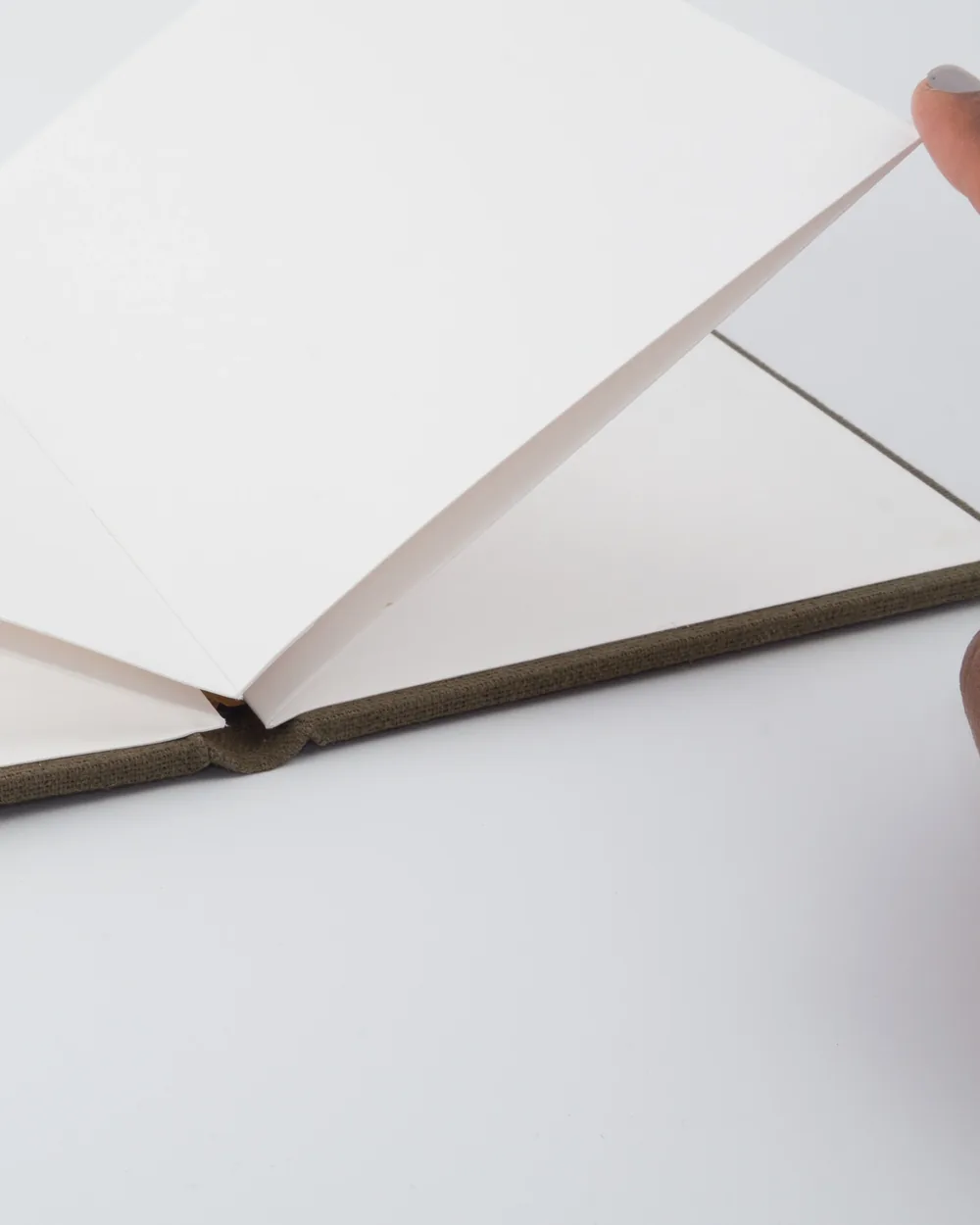 Open blank notebook with white pages on a white surface, someone turning the page with their right hand.