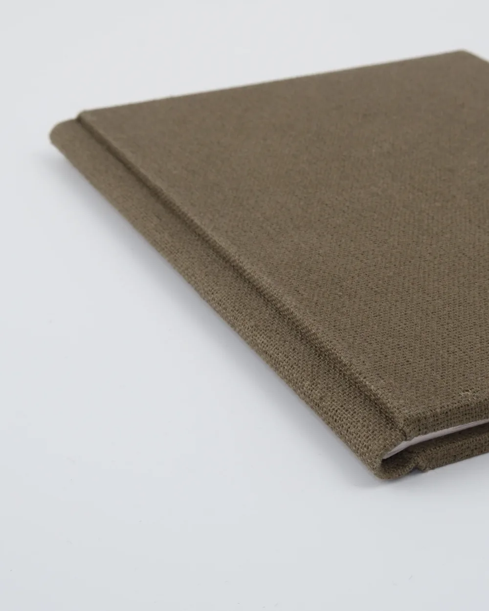 Close-up of a brown fabric-bound notebook with a white page corner visible, on a white surface.