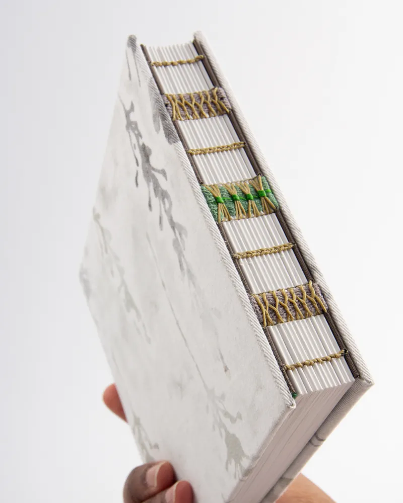 A person holding a thick book with a decorative cover and embedded built-in white sticks with colorful ties along the side.