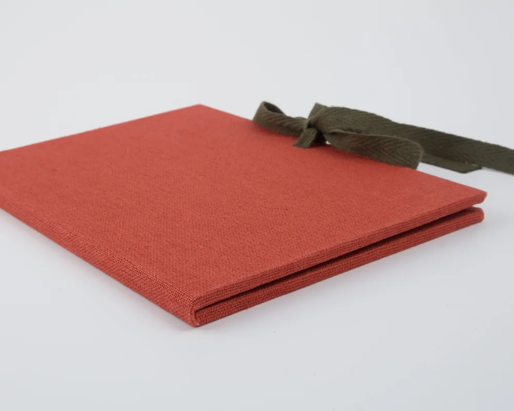 A red fabric notebook with a green ribbon tied in a bow on the upper right corner, placed on a white surface.