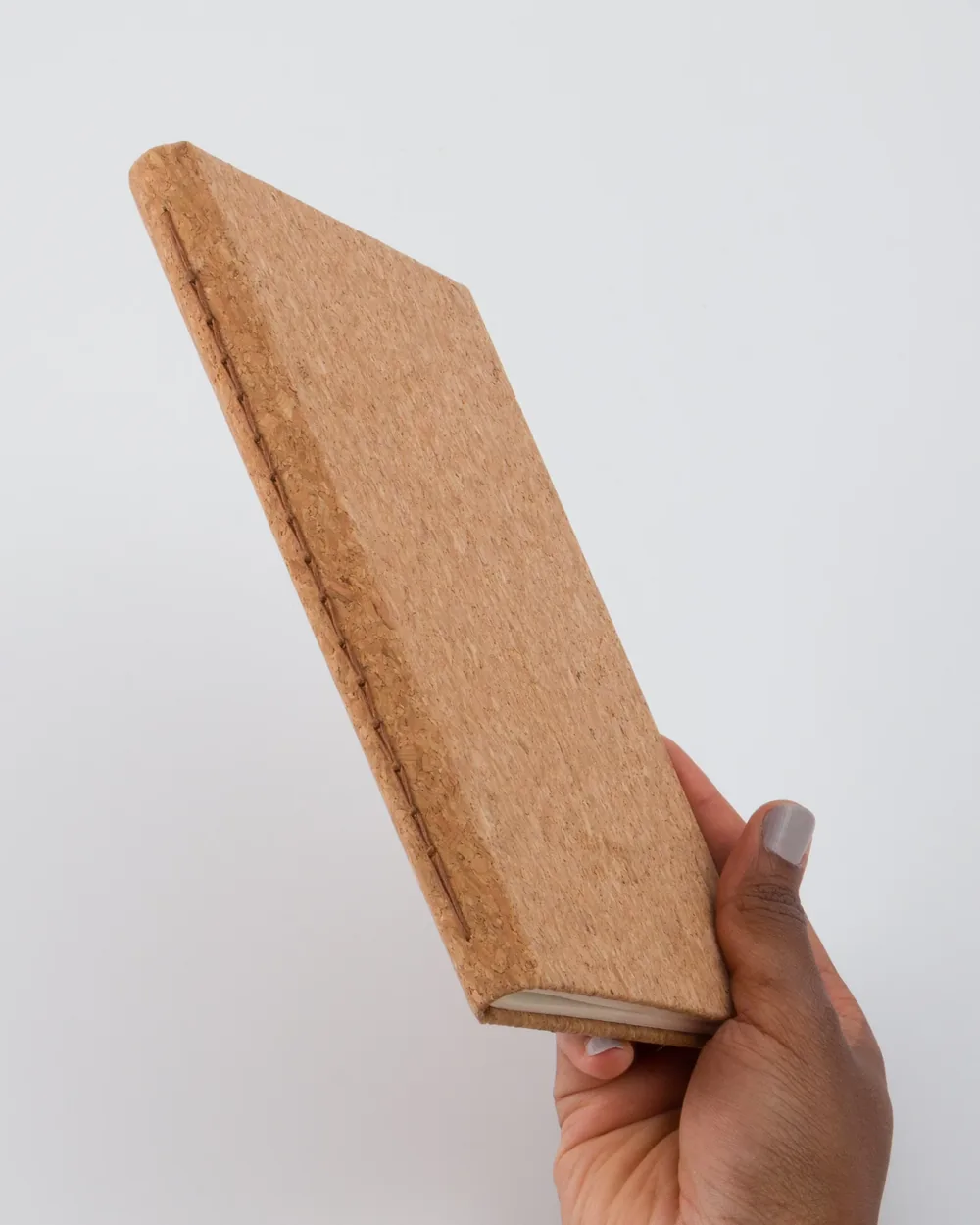 Hand holding a blank, textured, brown cork-covered book or notebook against a plain white background.
