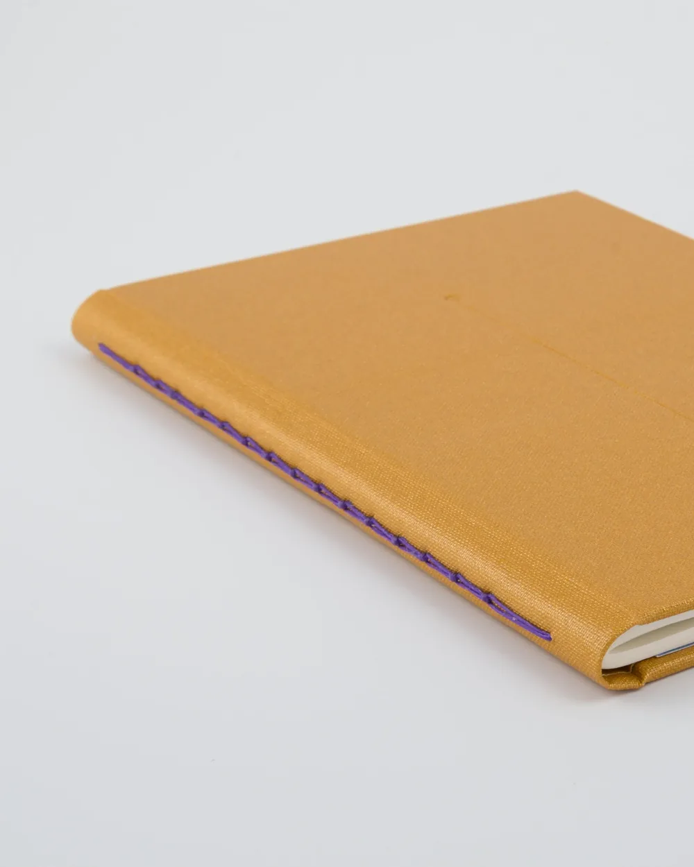 A closed, tan hardcover notebook with purple stitching on a white background.