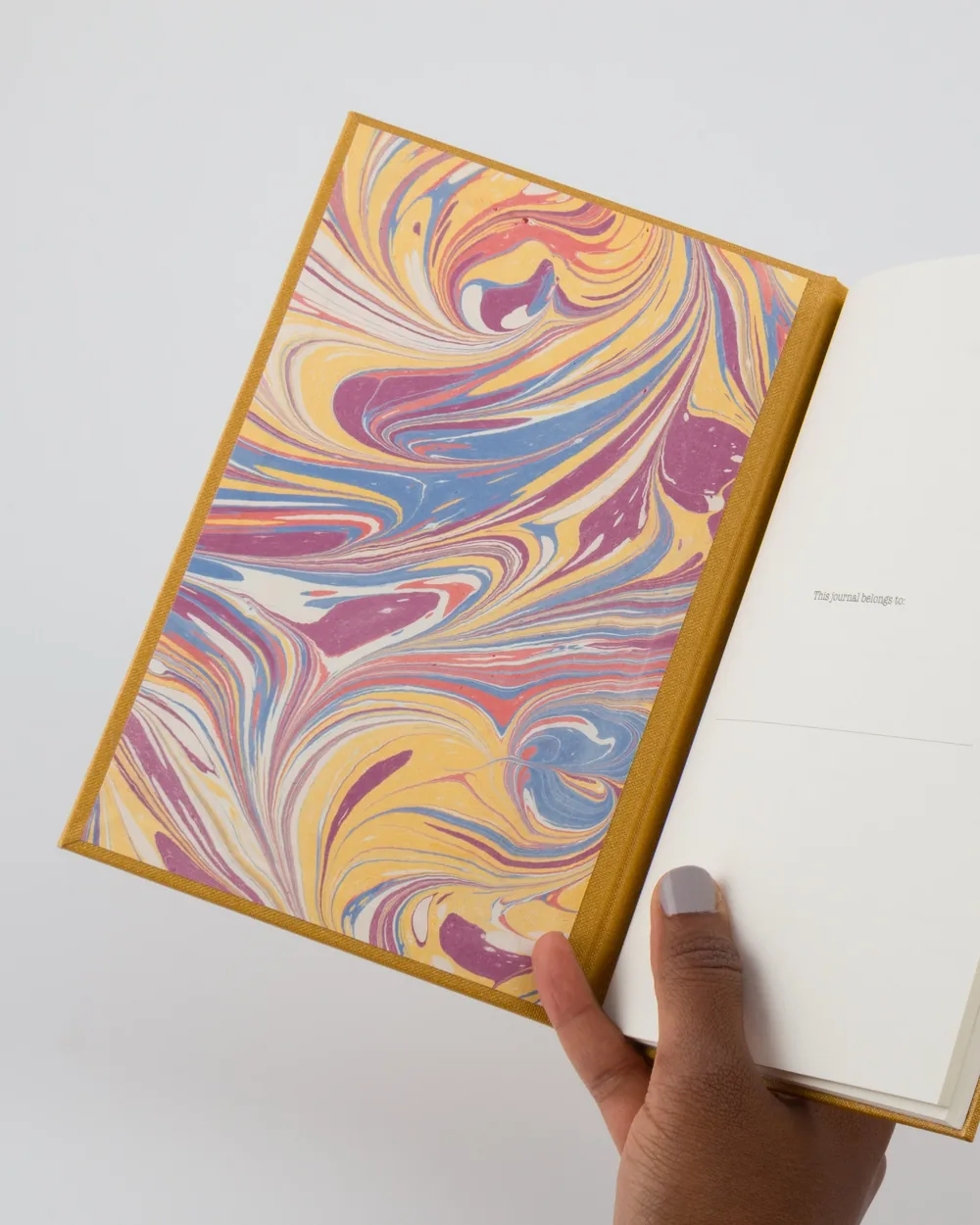 Open journal with a colorful marbled page on the left and a blank page on the right, with a hand holding the bottom corner.