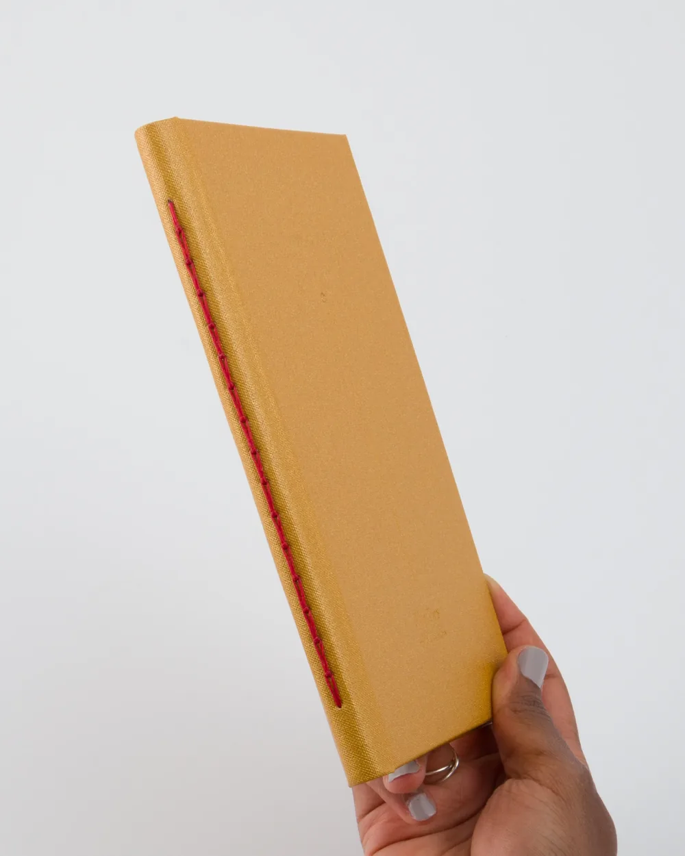 Person holding a tan hardcover book with red stitching along the spine against a white background.