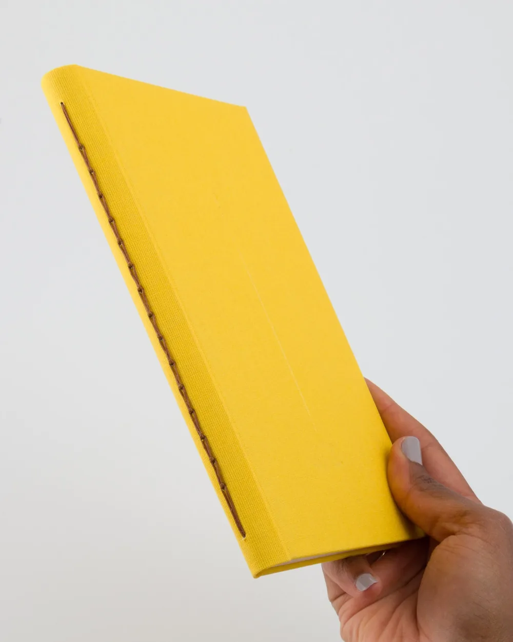 A person holding a closed yellow hardcover book with a textured surface and visible binding on the left edge.