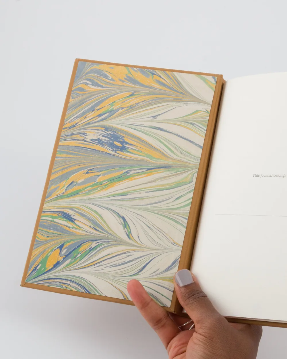 Open journal with colorful marbled page on the left and blank right page with text 'This journal belongs'