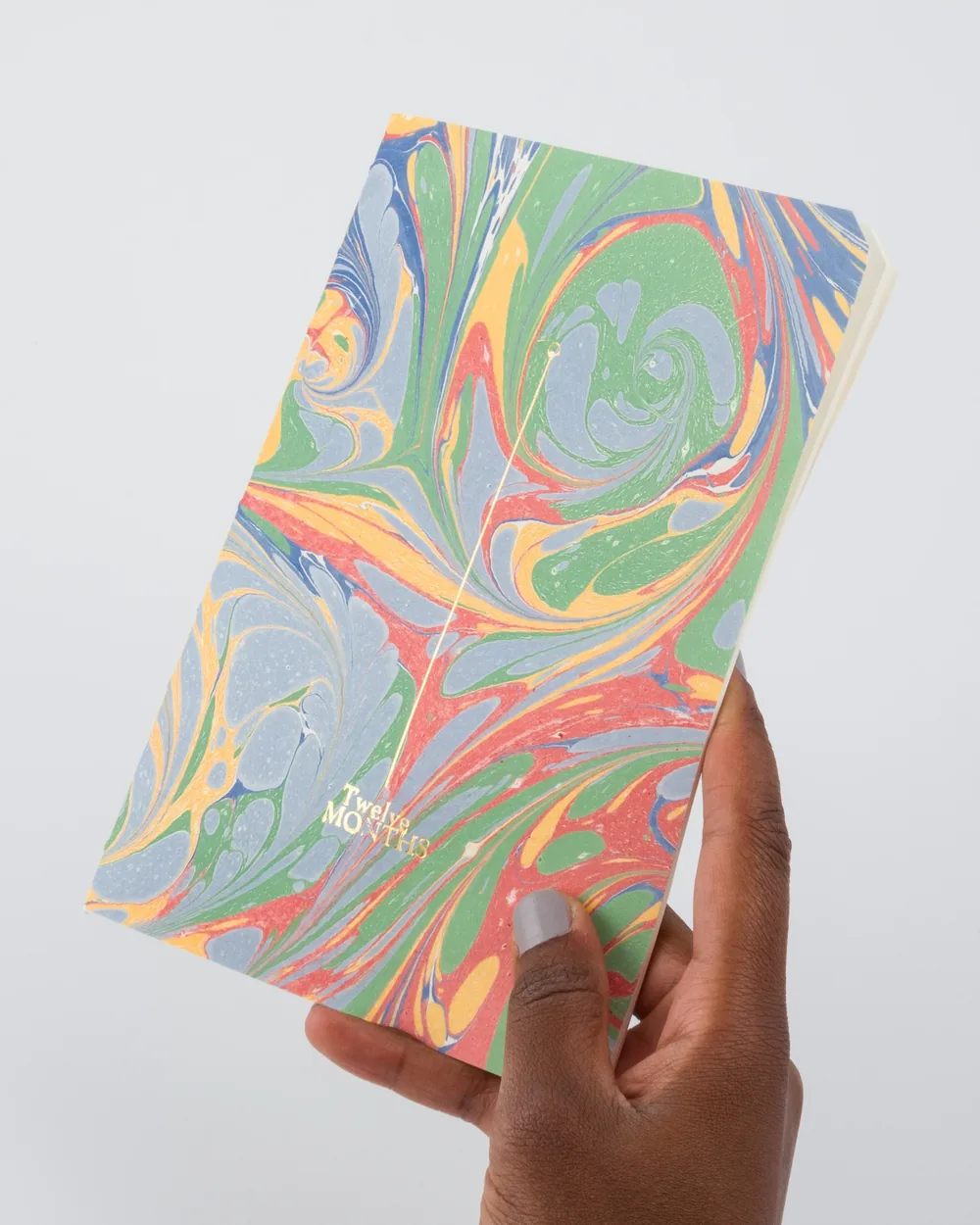 A person's hand holding a colorful marble-patterned 12-month planner.