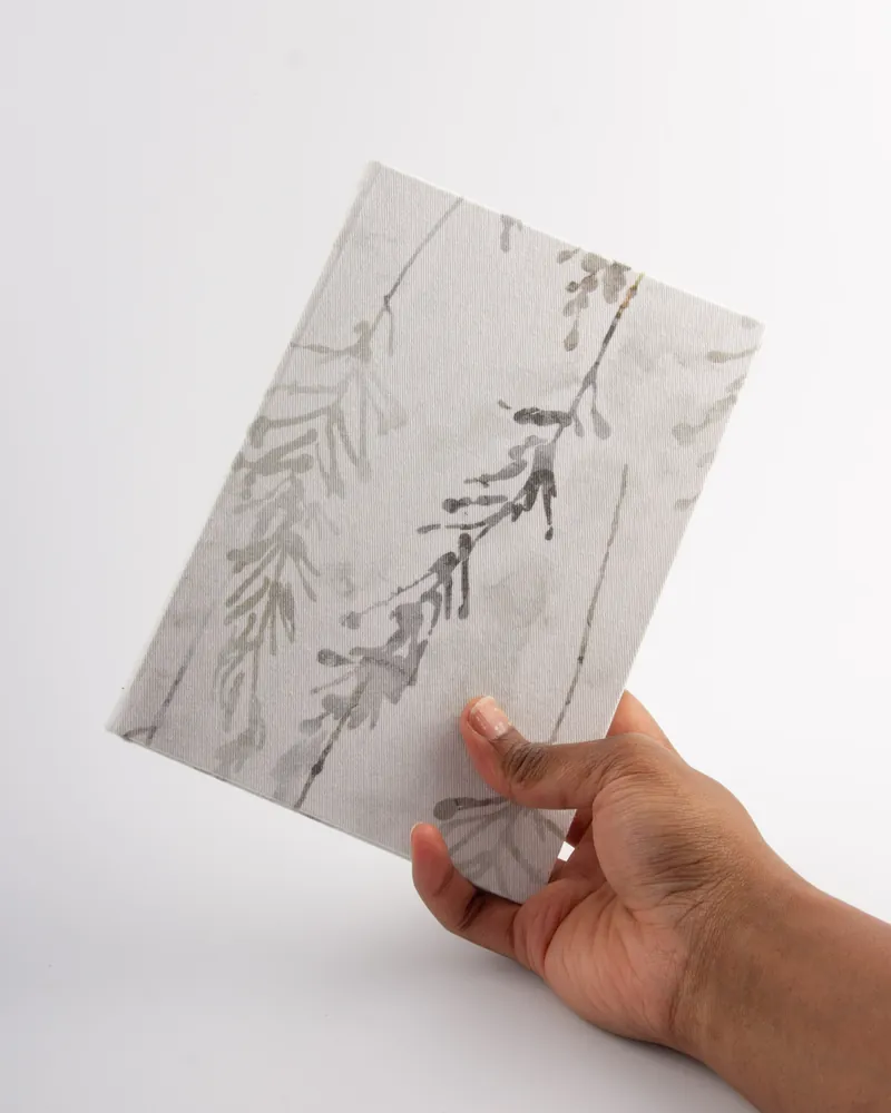 Hand holding a white gift box with a gray botanical design on a plain white background.