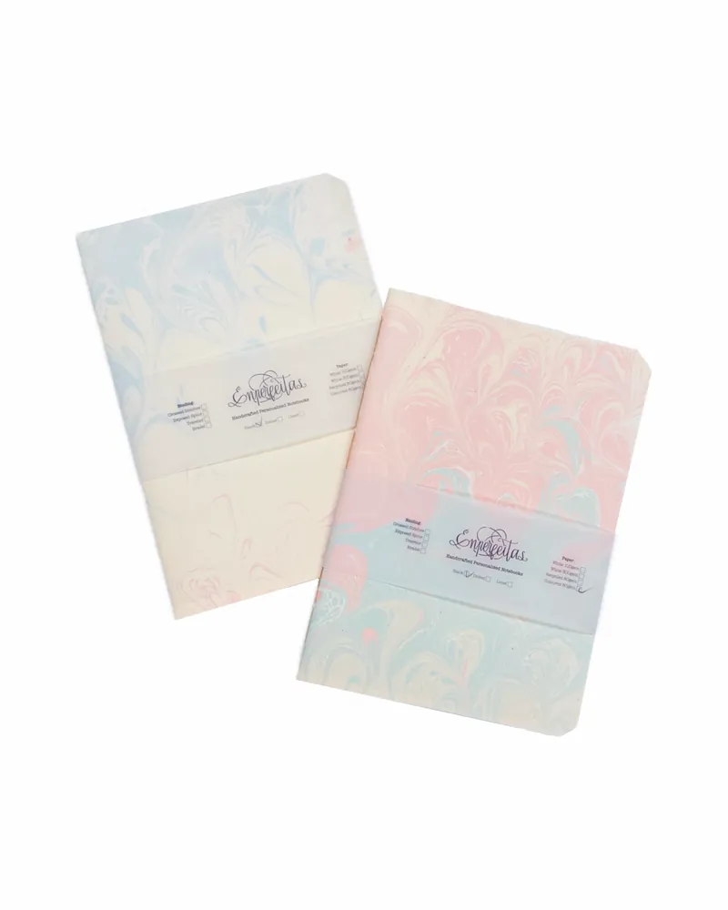 Two pastel-colored marble-patterned notebooks, one in light blue and the other in pink, with the brand name 'Emperletas' on the covers.
