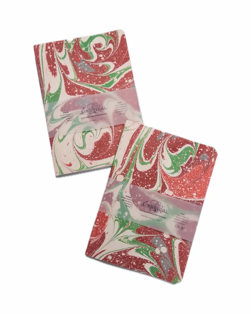 Two marbled soap bars with red, green, and white patterns, sealed with a translucent label showing a brand name and instructions.