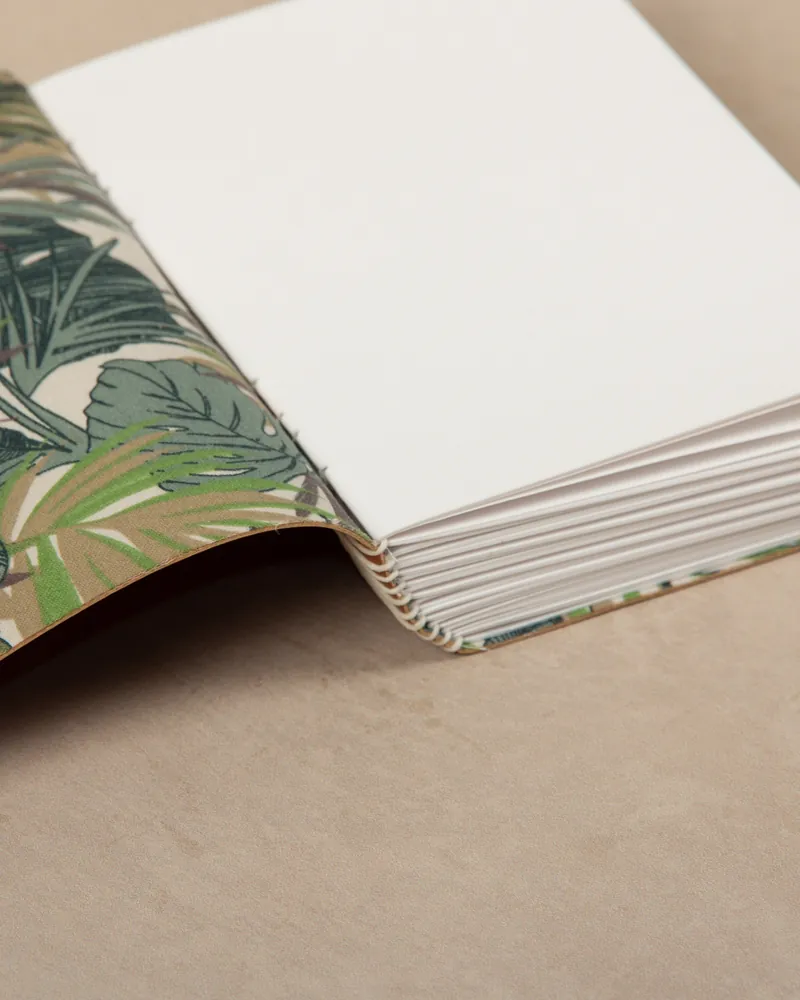 Open notebook with blank white pages and a tropical leaf pattern on the cover, resting on a beige surface.
