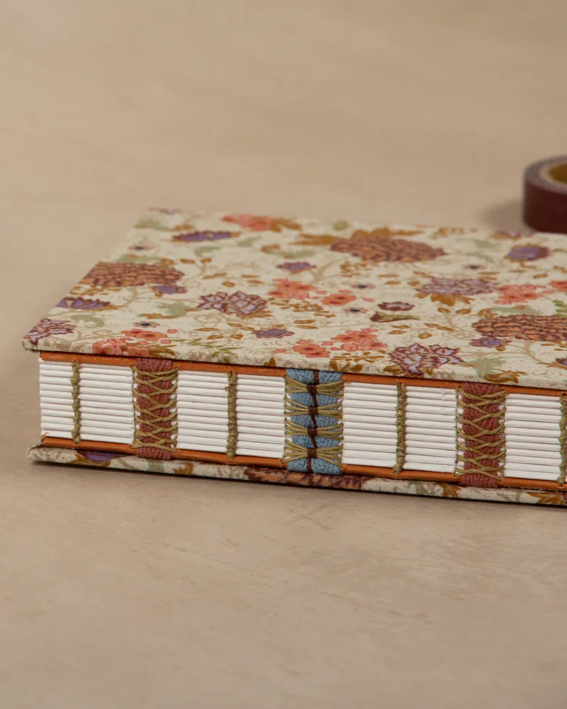 A hardcover book with a floral patterned cover, showing the side and spine with visible stitching and a roll of tape in the background.