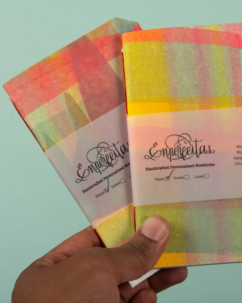 Two colorful notebooks with a rainbow-colored cover, held in a person's hand. The notebooks feature the brand name 'Emprejetas' and are labeled as handcrafted personalized notebooks, with options for blank, dotted, or lined pages.