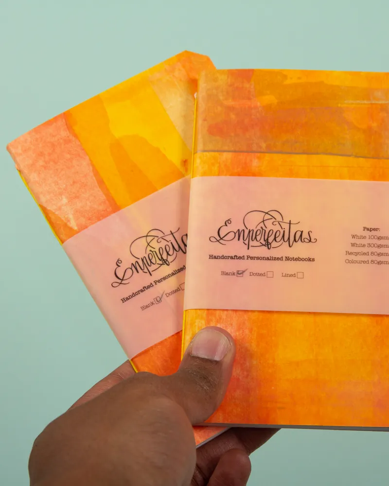 Two colorful notebooks with a label that reads "Empeignetas Handcrafted Personalized Notebooks" held by a hand against a light blue background.