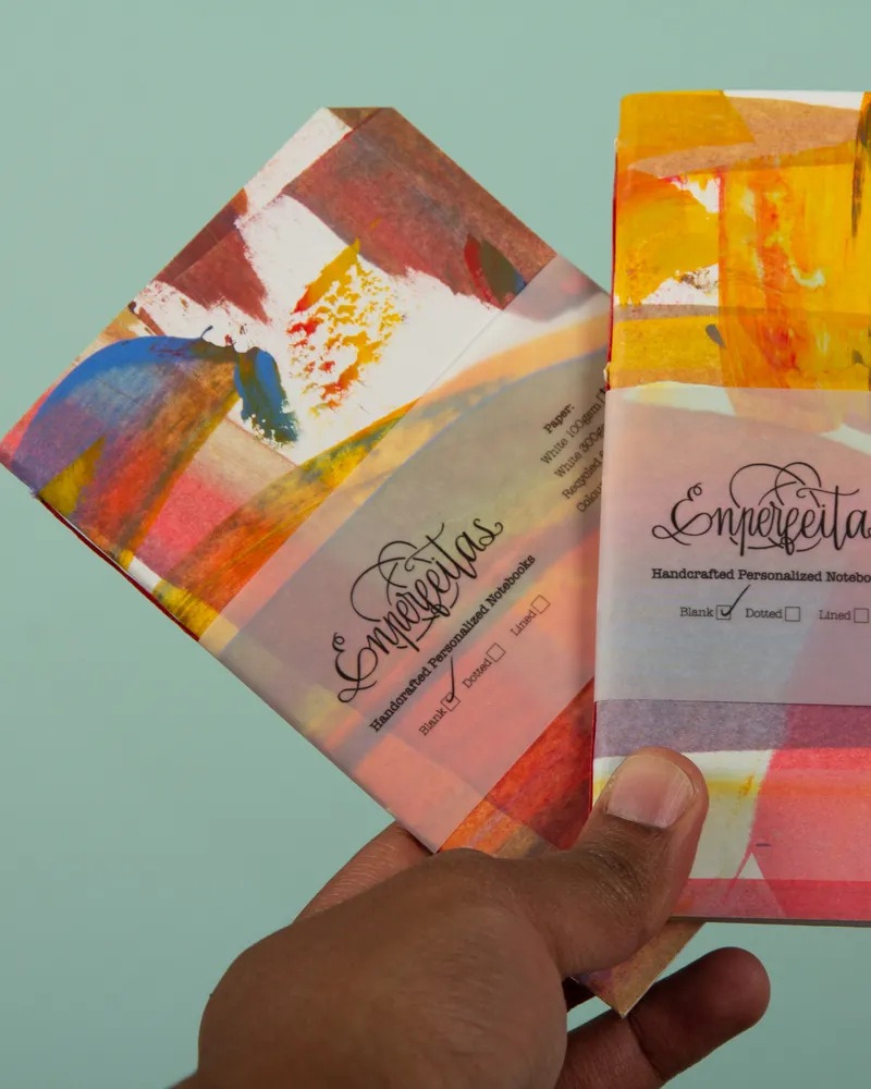 Close-up of two colorful, handcrafted personalized notebooks with abstract artwork on the covers, one being held by a person's hand.