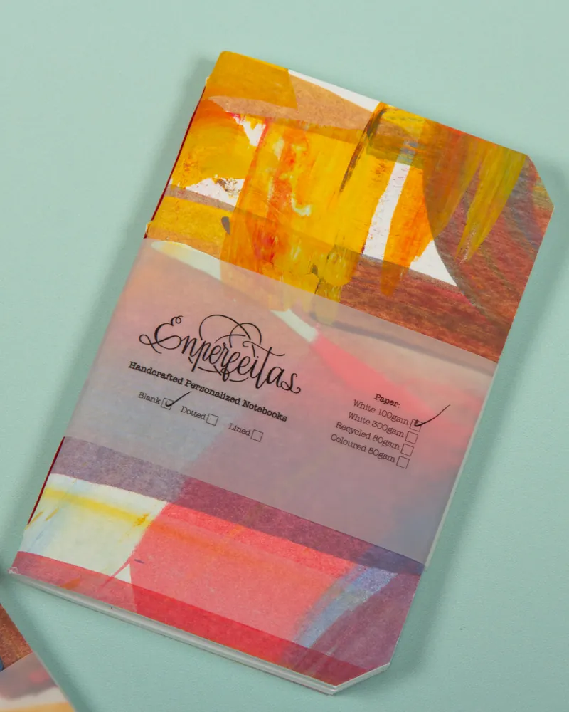 A packaged notebook with a colorful abstract cover design and a translucent band with the brand name 'Snerquetas' printed on it, placed on a light blue surface.