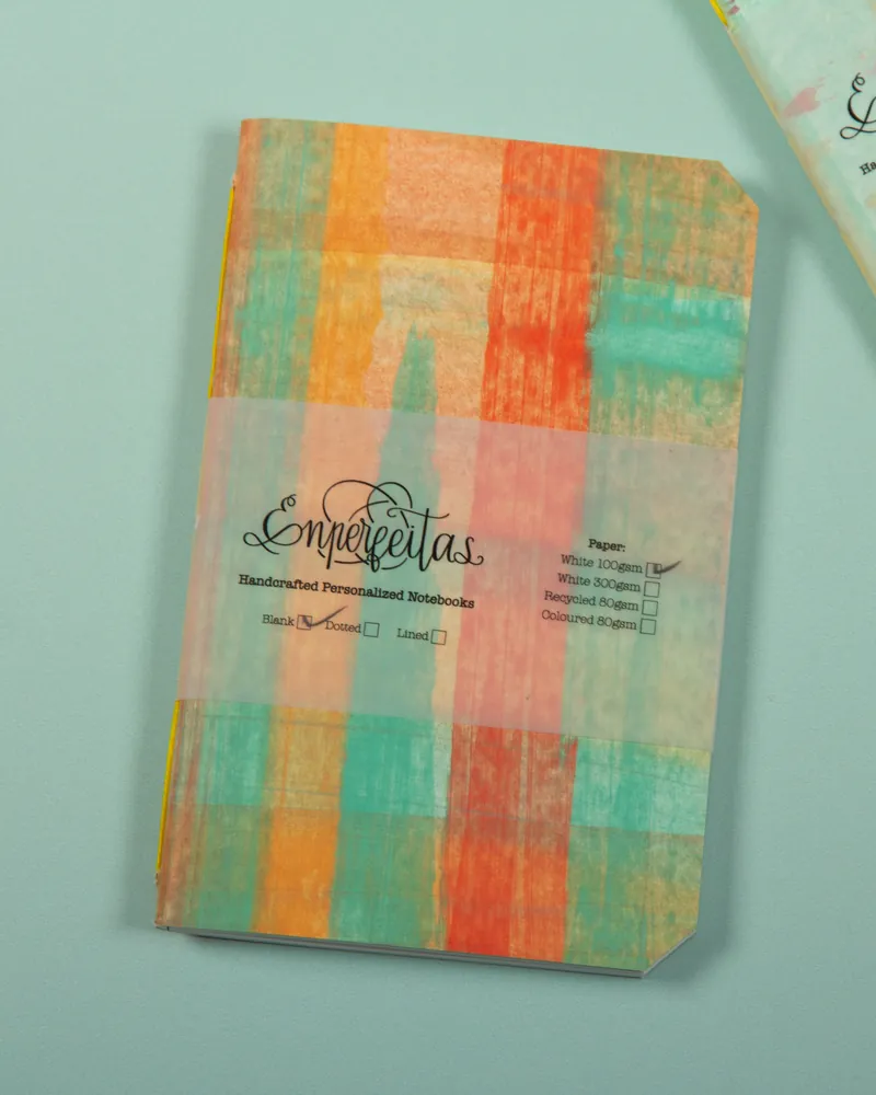 Colorful notebook with abstract pastel cover and transparent band with handwritten-style text and checkboxes on a light teal background.